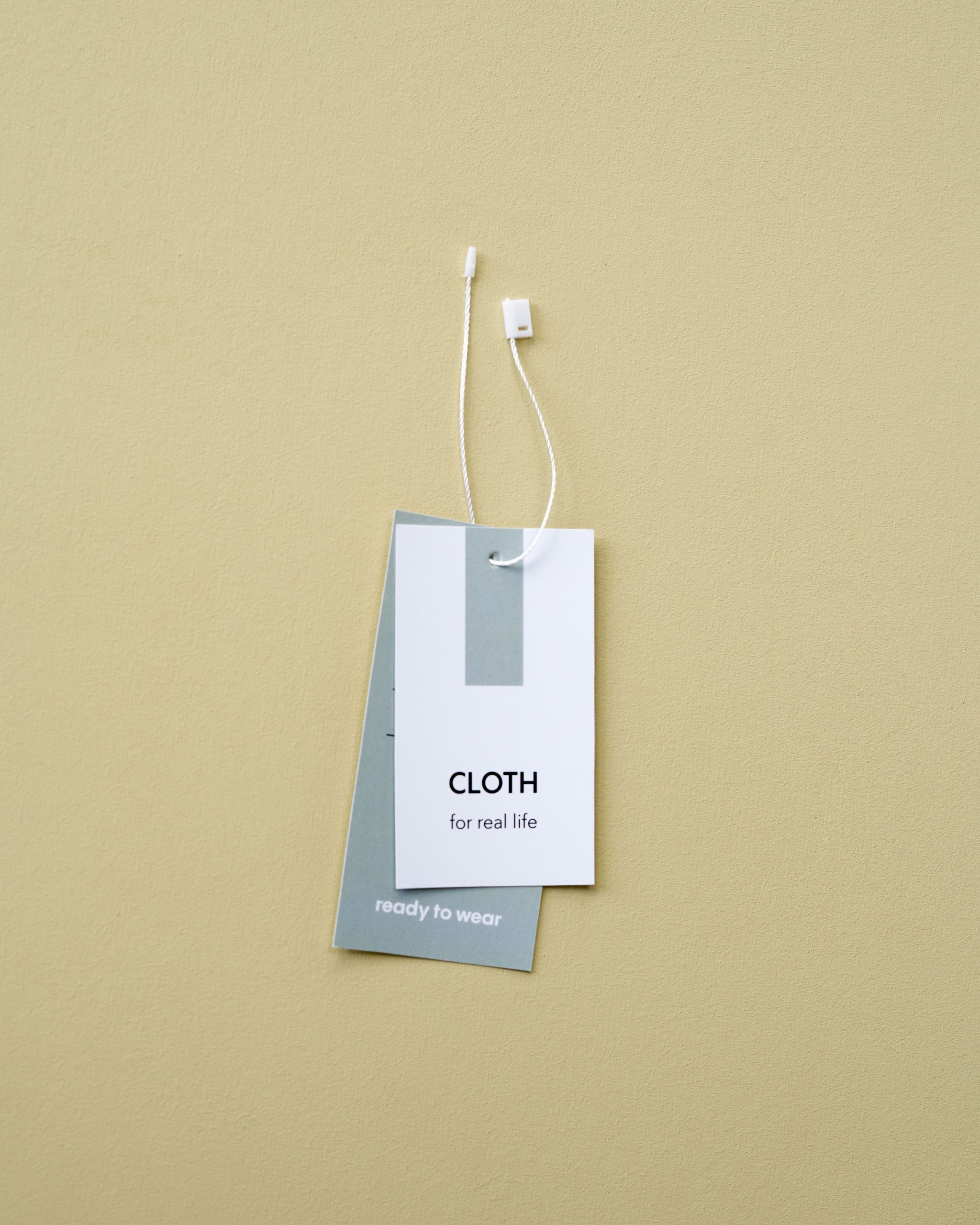 Close-up of minimalist clothing labels against a beige backdrop, featuring 'CLOTH for real life'.